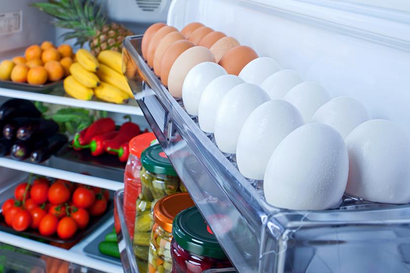 open refrigerator with eggs in the door and bananas pineapple eggplant peppers tomatoes oranges